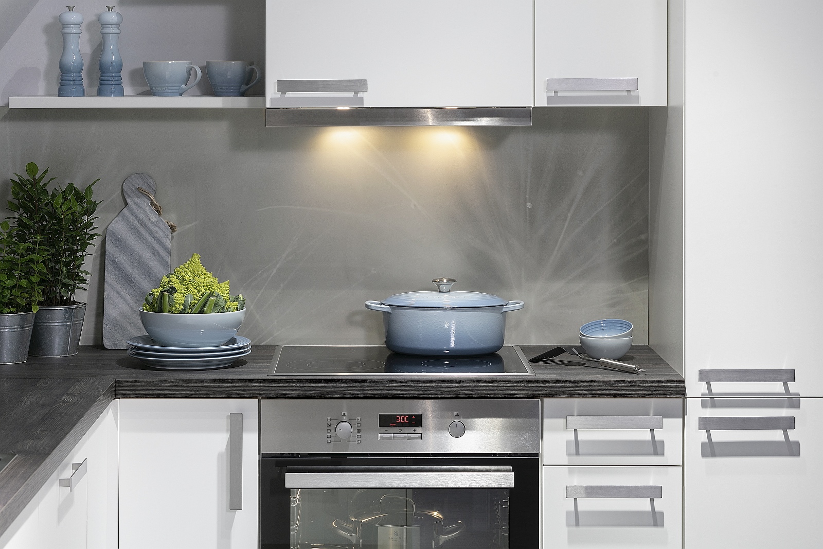 Weiße L-Küche mit grauer Nischenrückwand und dekorativem hellblauem Geschirr