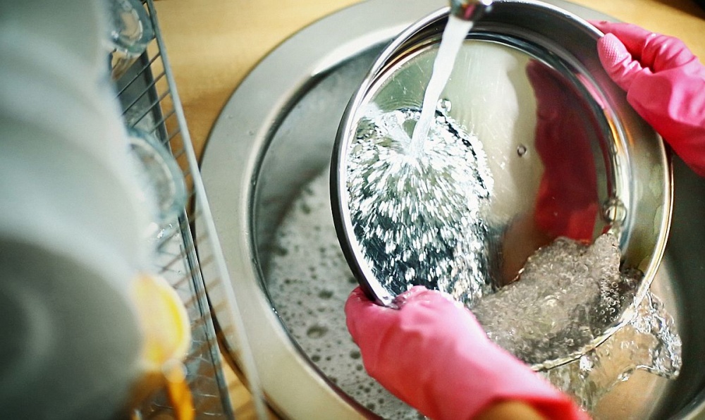 Abspülen in der Küchenspüle unter fließendem Wasser mit Gummihandschuhen