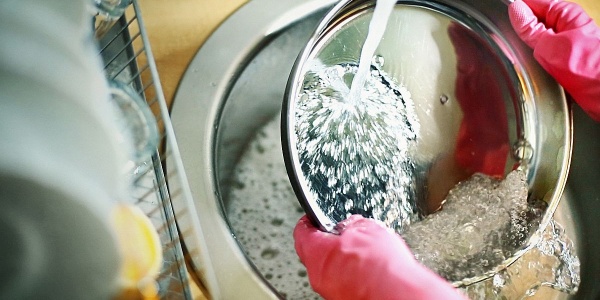 Abspülen in der Küchenspüle unter fließendem Wasser mit Gummihandschuhen